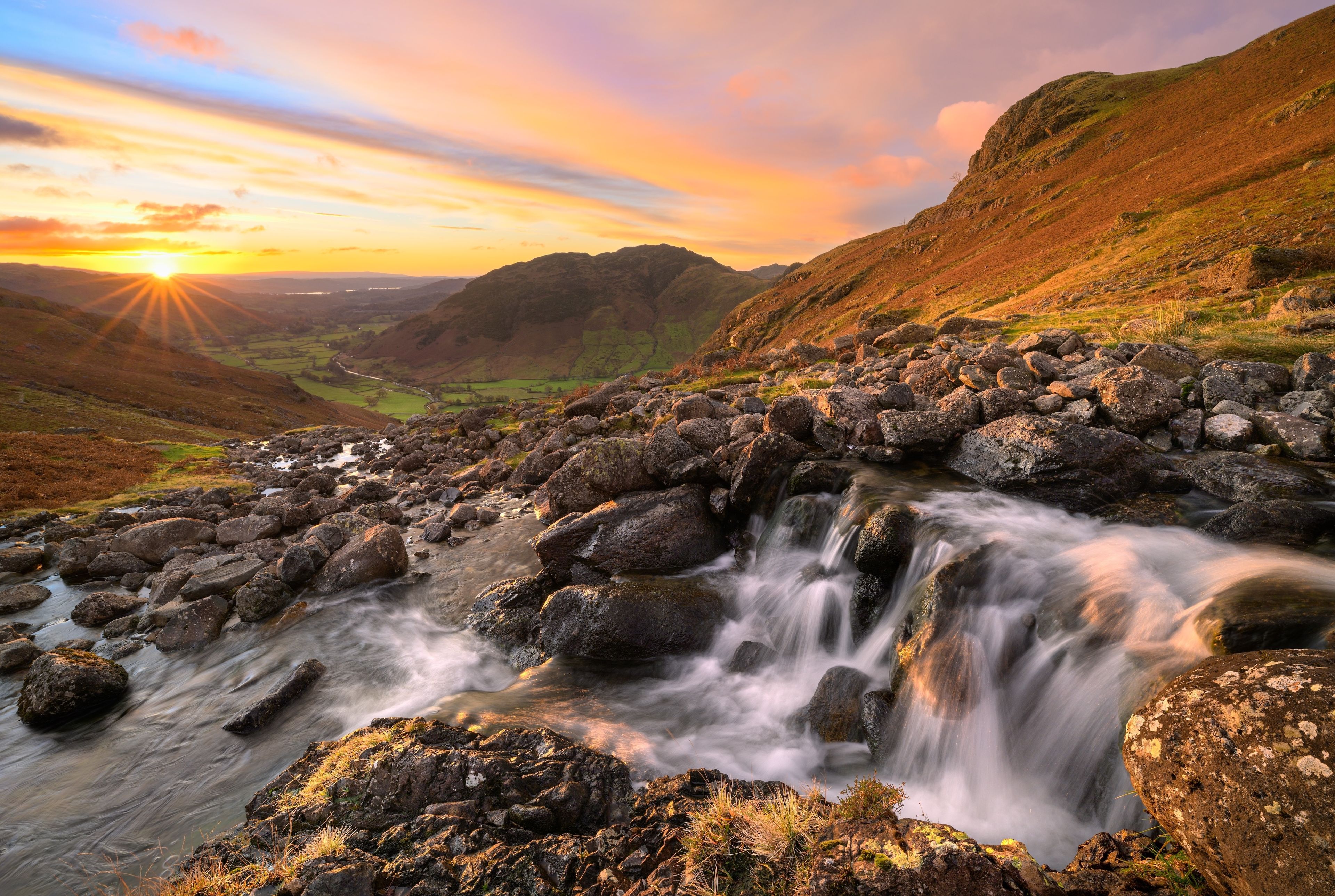 Beautiful sunrise in Lake District mountains with flowing waterfall.